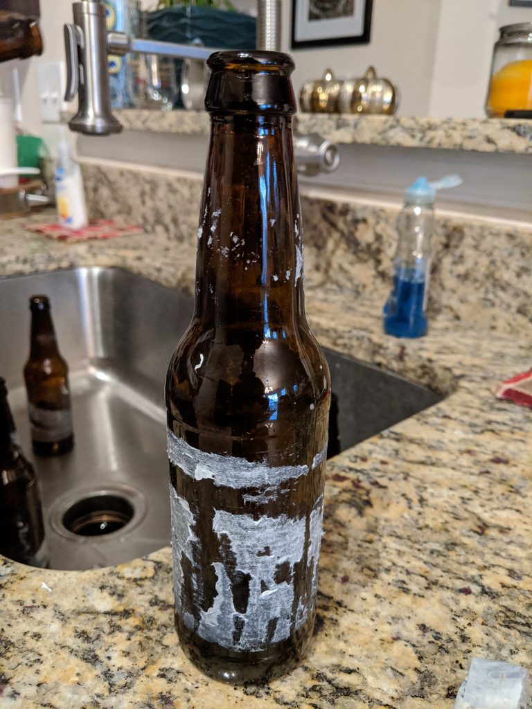 An image of a beer bottle with the label removed, showing remaining paper and glue residue.