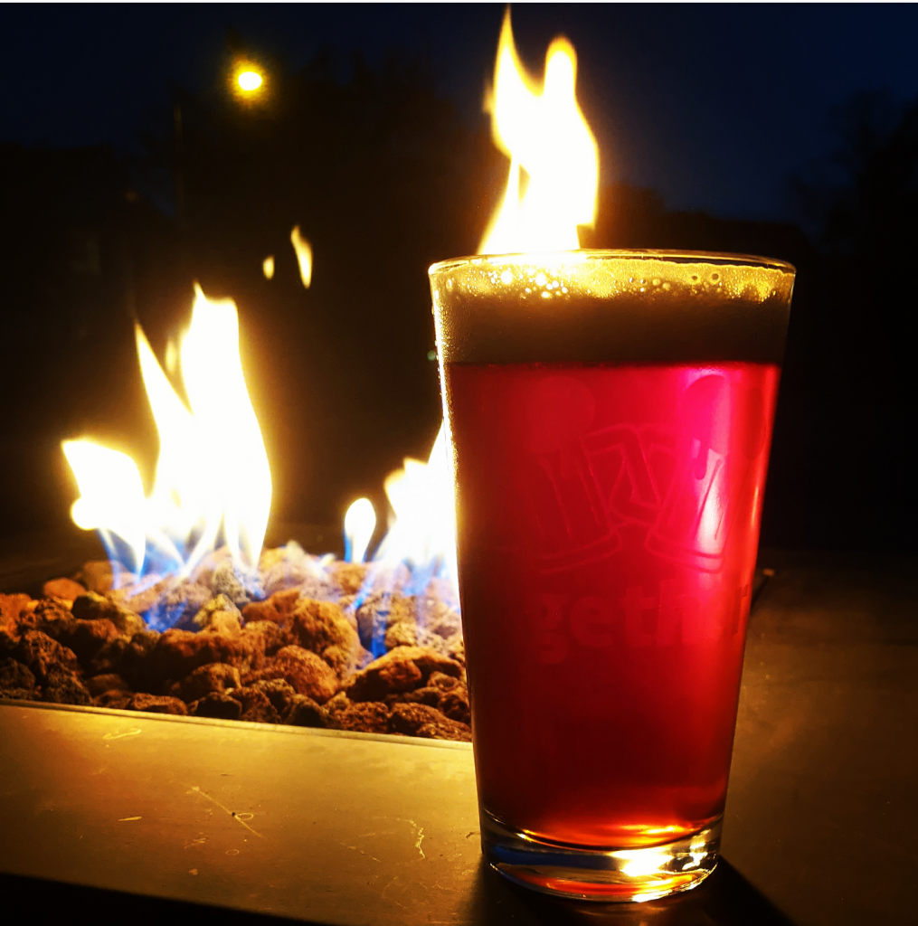 A pint of Smoke Signal IPA in front of a fire.
